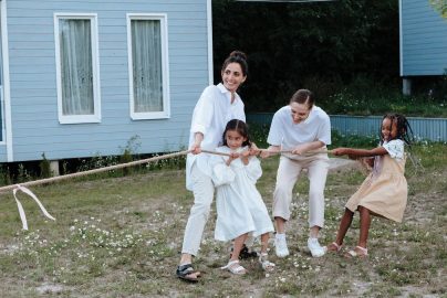 A happy family enjoys a game of tug of war in a grassy field by a house.