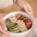 Delicious smoothie bowl topped with fresh fruits like kiwi, banana, and strawberries, held by manicured hands.