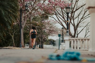 A woman jogs through a picturesque park lined with blooming spring trees and vintage lamps.